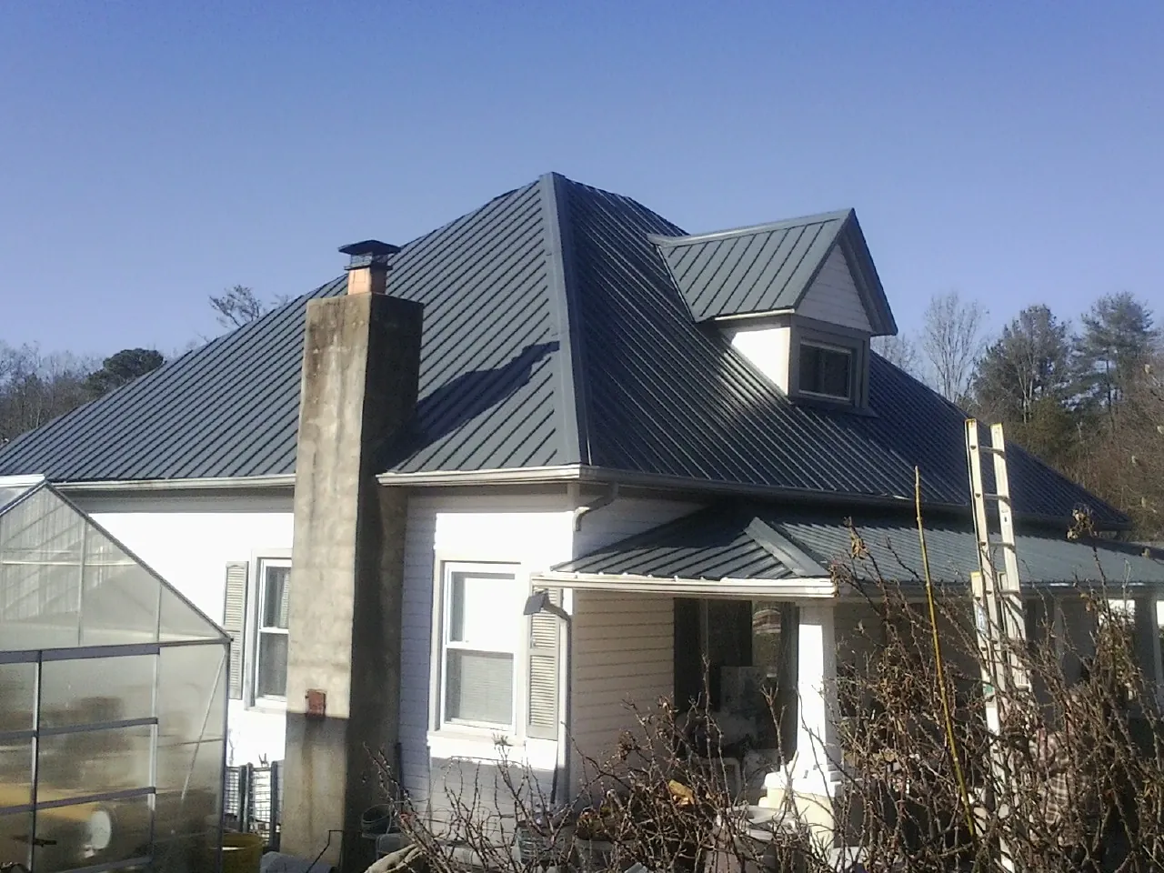 Dark blue standing seam metal roof on a white farmhouse with dormer — Slate & Tile Roof Repair by Roofing Brothers in Fall Creek