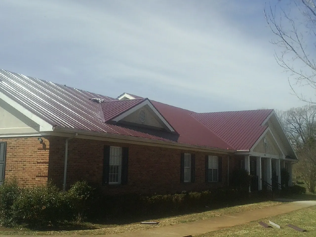 Red metal roof with gabled entries on a long brick building, from a Hail Damage Roof Repair job in Fall Creek
