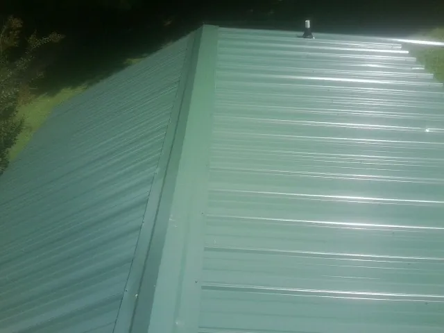 New green metal panels meeting at the ridge of a roof — Flat Roof Repair work by our crew in Fall Creek