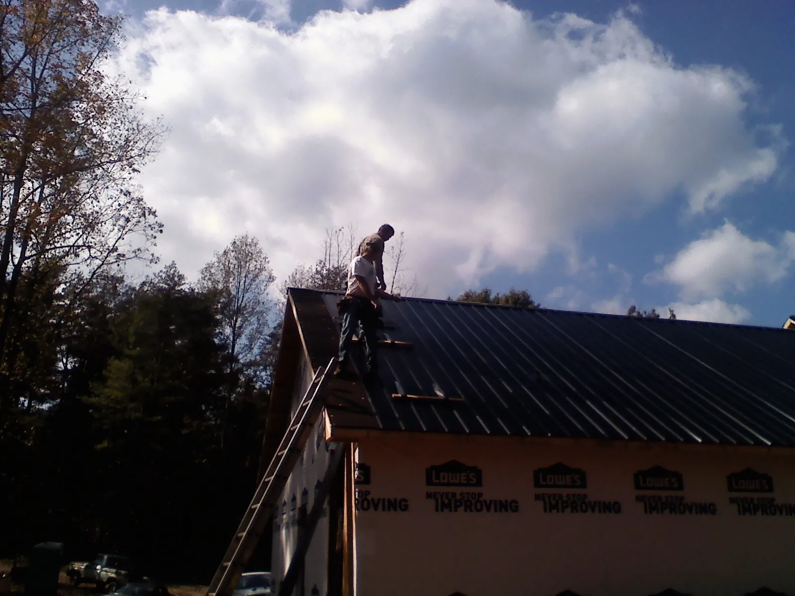 Roofer fastening dark metal panels high against a cloudy sky, from a Roof Inspection job in Fall Creek