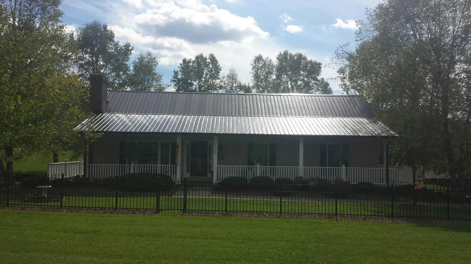 Gray metal roof on a brick ranch with a full width front porch — Gutter Guard Installation work by our crew in Fall Creek