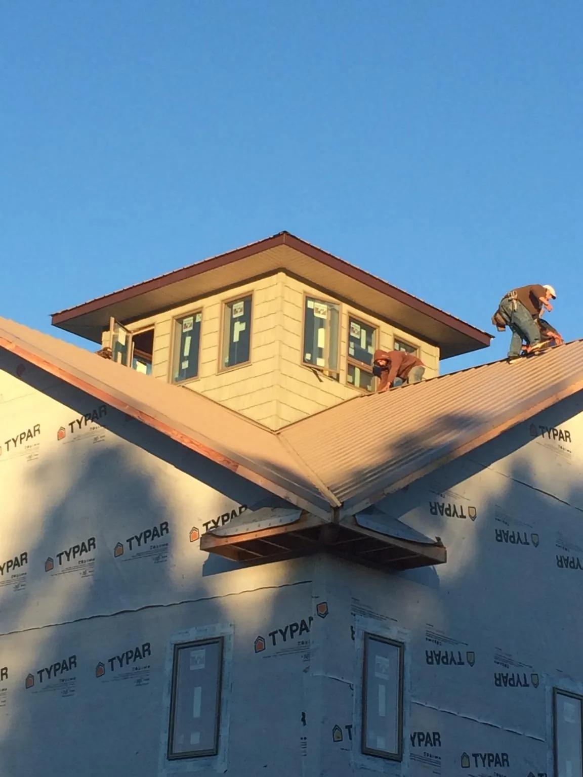 Roofers working around a rooftop cupola on a new metal roof at sunset — Roof Waterproofing in Fall Creek by Roofing Brothers